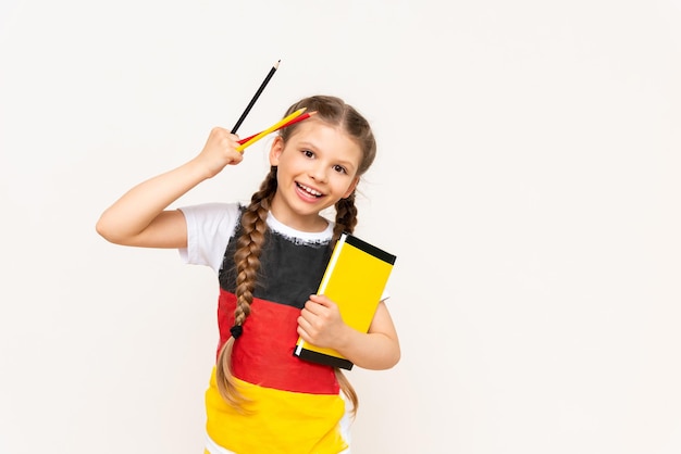 A little girl with a German flag on her Tshirt holds a book and pencils on a white isolated background German language courses for schoolchildren