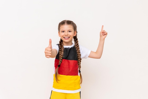 ピグテールの長い髪のTシャツにドイツ国旗を掲げた少女が、白い孤立した背景の広告に人差し指で指さします。語学コース