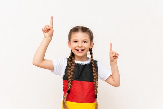 A little girl with a German flag on a Tshirt with long hair in pigtails points up with her index finger at your advertisement on a white isolated background Language courses