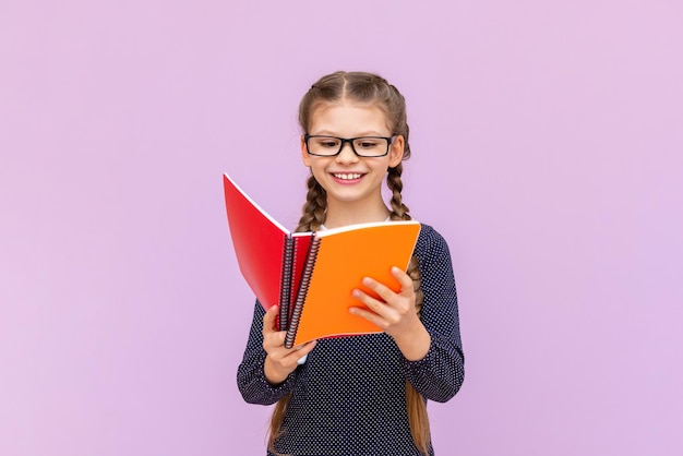 A little girl with glasses holds textbooks in her hands and smiles broadly on a pink isolated background Educational courses for schoolchildren