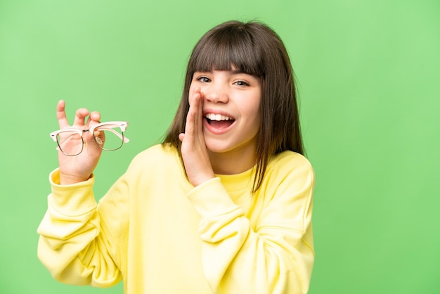 何かをささやく孤立したクロマキーの背景の上に眼鏡をかけた少女