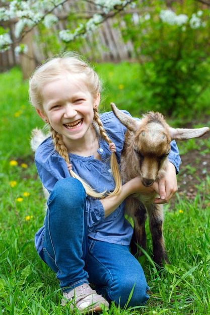 Little girl with a goatling in the garden, spring