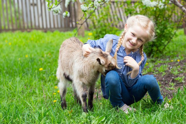 Little girl with a goatling in the garden, spring