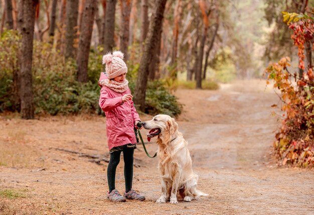 Bambina con il cane golden retriever scappando nella foresta di autunno colorato