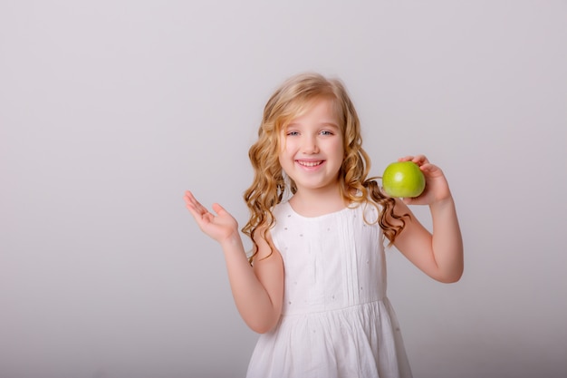 маленькая девочка с зеленым яблоком в руках сладко улыбается