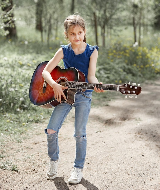 Little girl with guitar standing on the path in the city Park