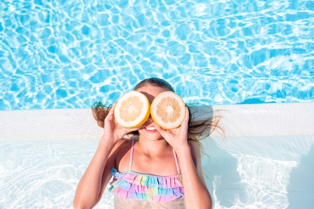 Little girl with halves citrus lemons in swimming pool