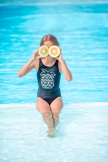 Little girl with halves citrus lemons in swimming pool