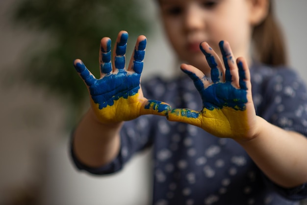 Маленькая девочка с руками в красках желтого и синего украинского флага символически показывает на камеру