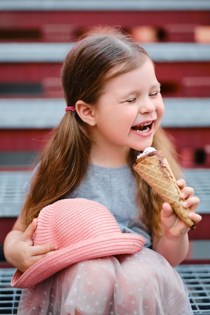 Маленькая девочка в шляпе ест мороженое