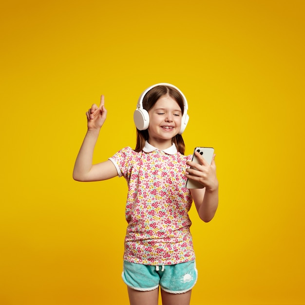 Little girl with headphones pointing index finger up holding mobile phone