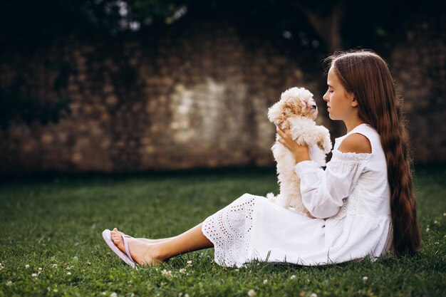 彼女の家の裏庭で芝生の上に座っているマルチパ犬を持つ少女