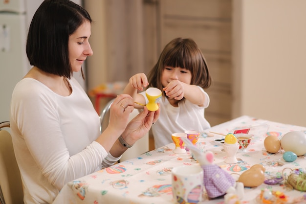 Little girl with her mom preparing for easter and print eggs they are sitting by the table and have