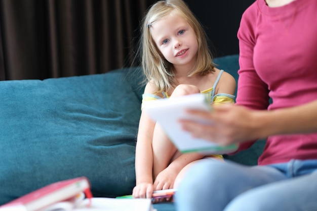 A little girl with her mother are sitting on the couch with books