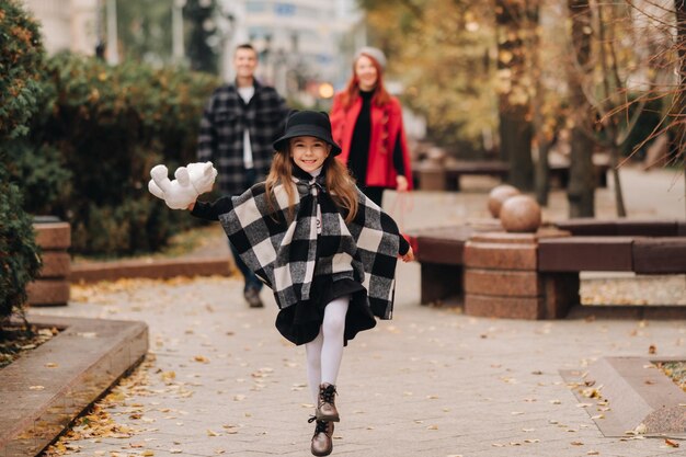 A little girl with her parents runs to the autumn cityA stylish family of three strolls through the autumn city
