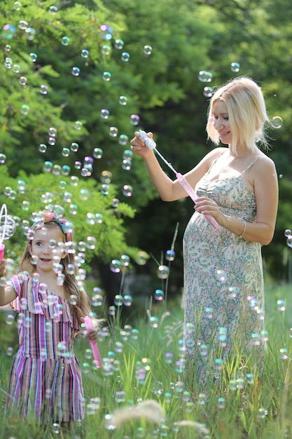 Photo little girl with her pregnant mommy have fun blowing bubbles