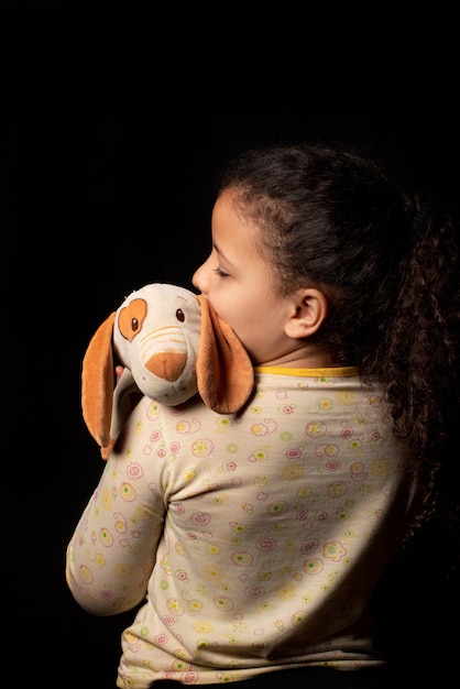Little girl with her stuffed animal, black background, Low Key portrait, selective focus.