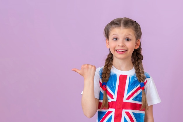 Foto una bambina con l'immagine della bandiera inglese su una maglietta punta il dito a lato del tuo annuncio. copia spazio.