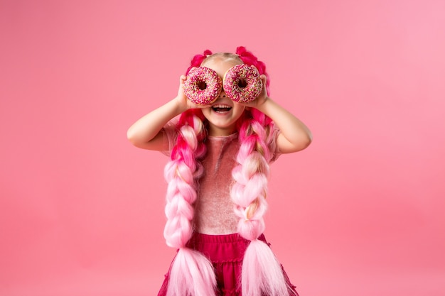 маленькая девочка с канекалон косичками с пончиками на розовом фоне