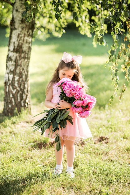 Bambina con un grande mazzo di peonie. un bambino cammina nel parco con i fiori in estate.