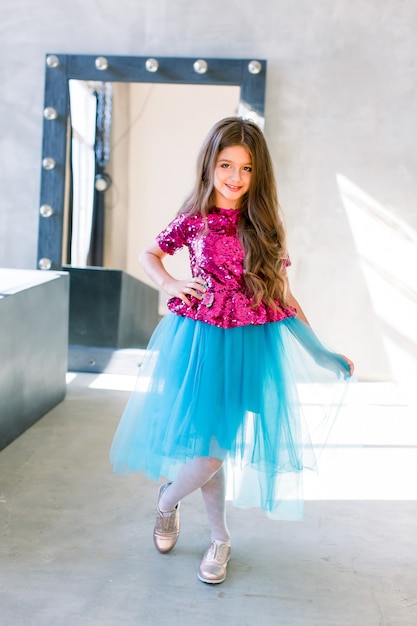 Little girl with long Brown hair dancing, smling and having fun over grey loft wall background. Five years old female child posing.