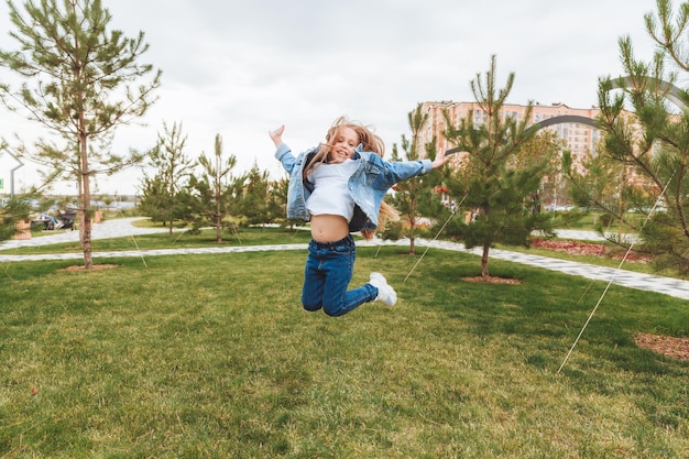 A little girl with long hair jumps having fun on the street The concept of a happy childhood