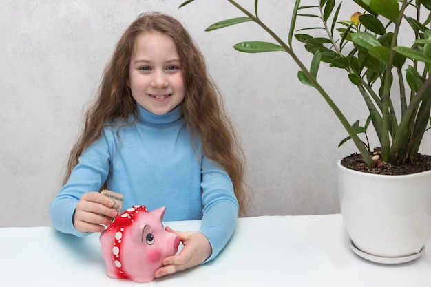 Photo little girl with long hair puts money in a piggy bank