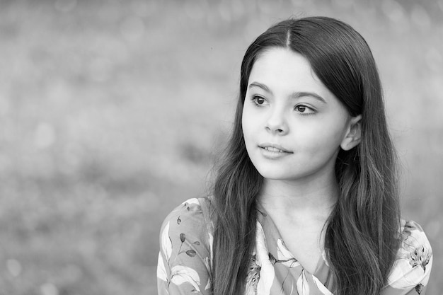 Little girl with long hair relaxing in park sunny day green grass background united with nature concept