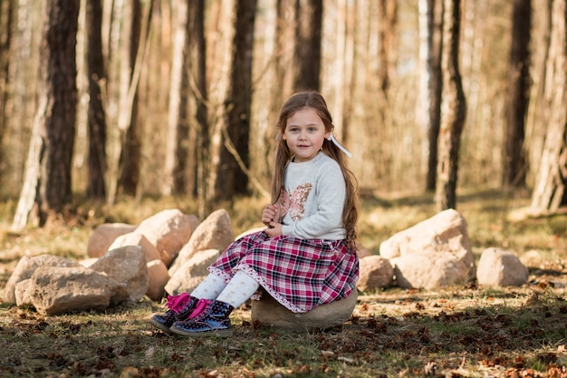маленькая девочка с длинными волосами сидит в лесу