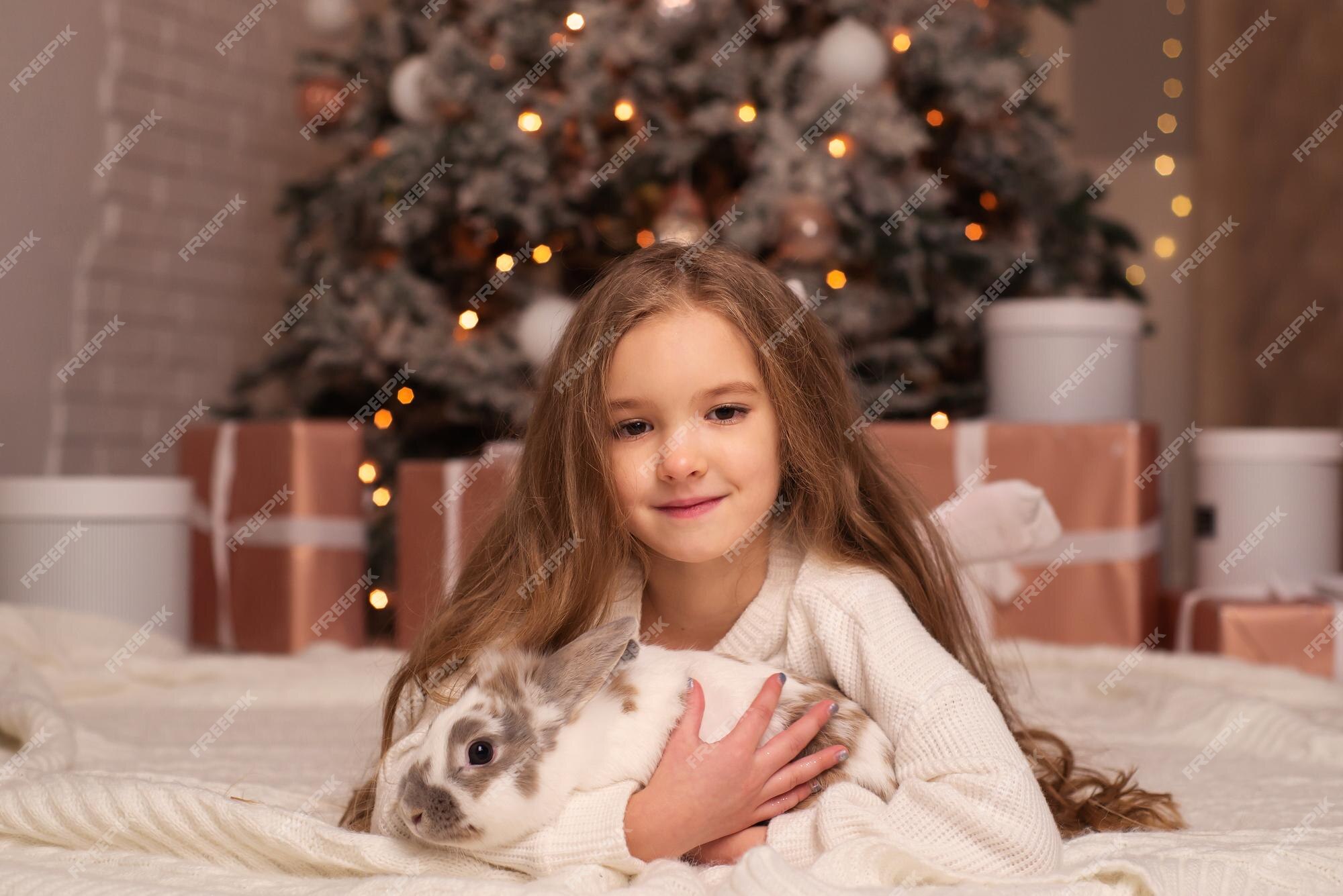 Premium Photo | Little girl with long hair in a sweater near the christmas tree with a rabbit in christmas at home Premium Photo | Little girl with long hair in a sweater near the christmas tree with a rabbit in christmas at home