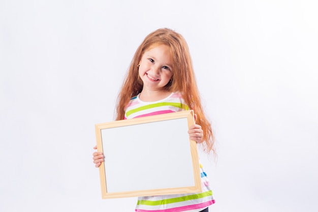 Little girl with long red hair is smiling and holding a white drawing board