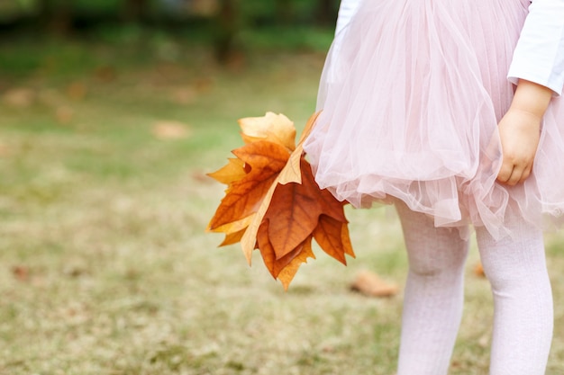 Little girl with maple leaf at autumn park.