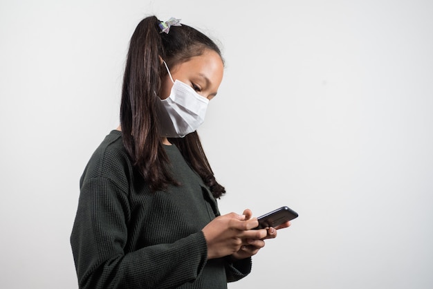 Little girl with medical mask looking at the mobile on white background