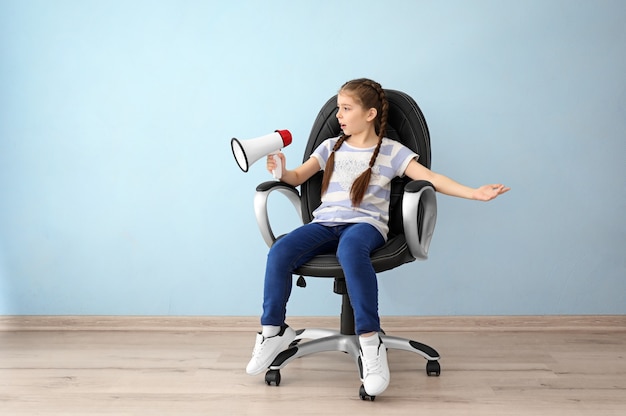 Маленькая девочка с мегафоном, сидя на стуле в пустой комнате