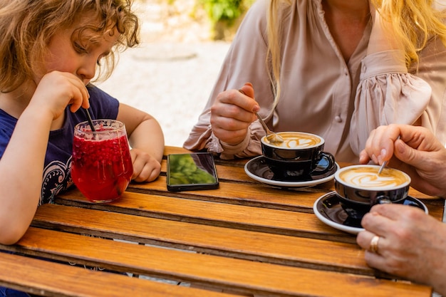 The little girl with mom and grandma drinks juice in a cafe