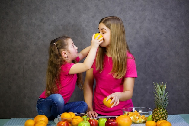 La bambina con la mamma gioca con la frutta e sorride. vitamine e alimentazione sana per i bambini.