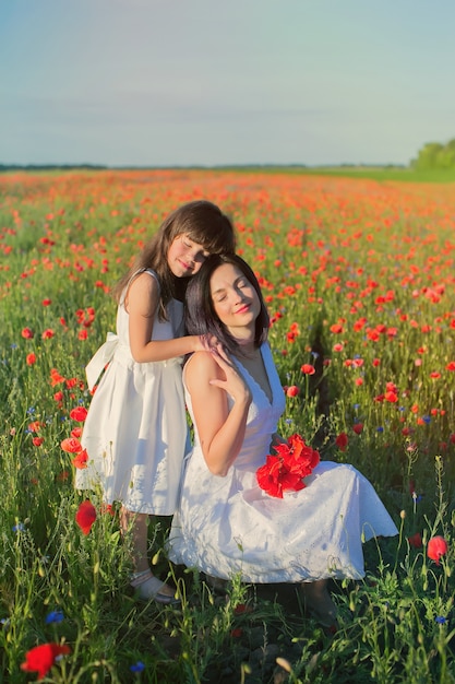 Little girl with mother in white dresses with bouquet of poppies .