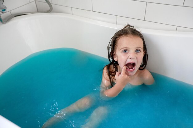 Little girl with mouth opened taking bath in bathtub