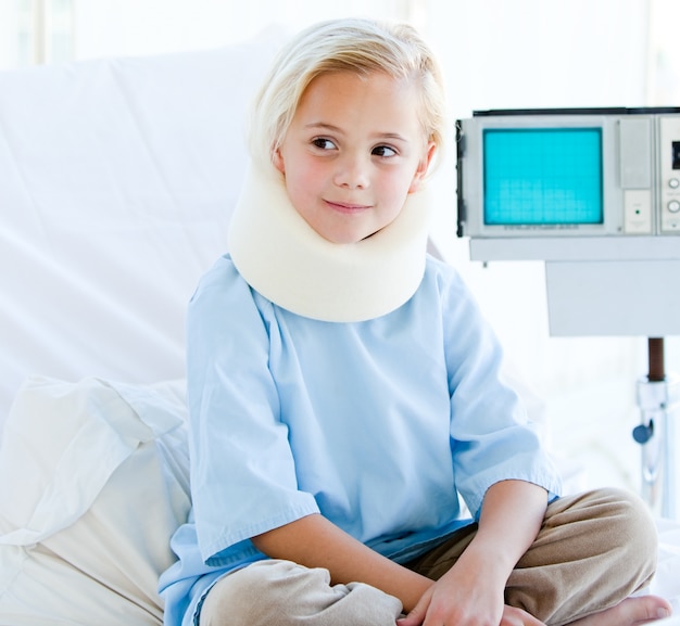 Little girl with a neck brace sitting on a hospital bed 