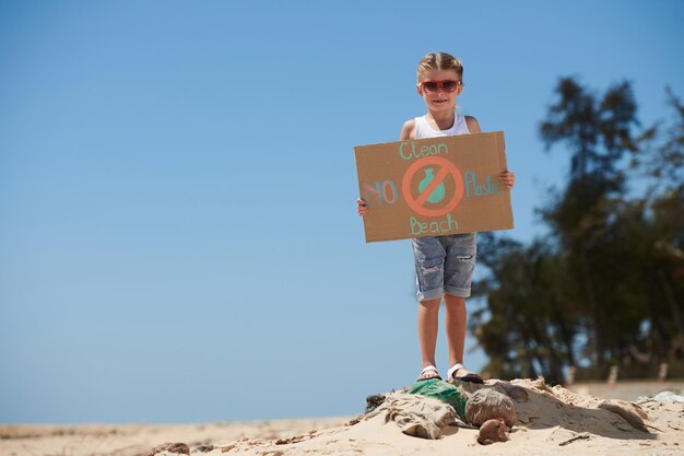 Bambina senza plastica e pulire il cartello della spiaggia in piedi sul mucchio di spazzatura sulla spiaggia