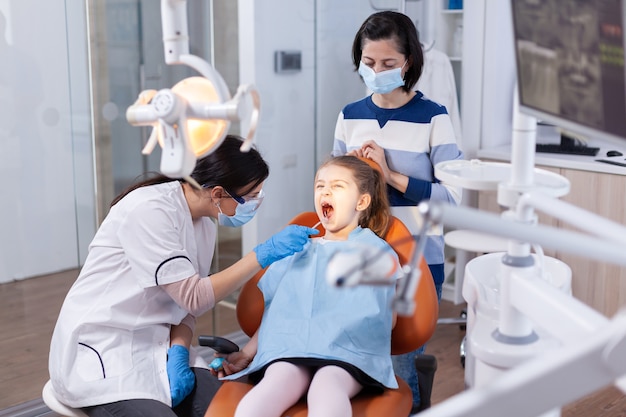 Bambina con la bocca aperta durante il controllo della cavità eseguito dallo stomatologo. specialista in odontoiatria durante la consultazione della cavità infantile nell'ufficio di stomatologia utilizzando la tecnologia moderna.