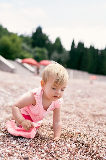 Little girl with a panama hat in her hand crawls along a pebble beach