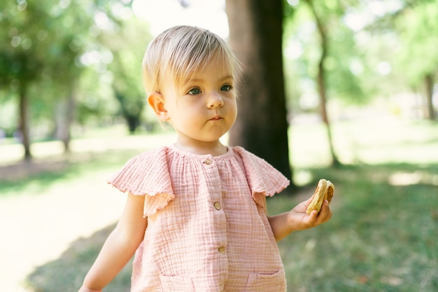 Маленькая девочка с блинчиком в руке стоит на зеленой лужайке