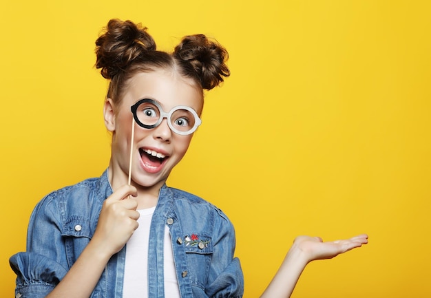 Little girl with a paper accessories over yellow background