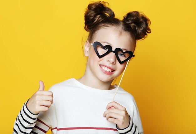 Little girl with a paper accessories over yellow background