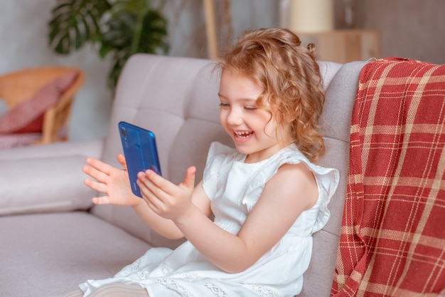 A little girl with a phone is sitting on the couch