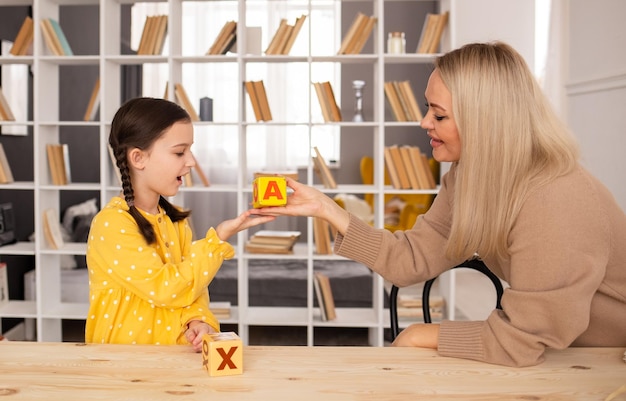 A little girl with pigtails has sex with a female speech therapist at a table in a room