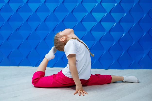 A little girl with pigtails in a white T-shirt on a blue background sits in twine on the floor and smiles. Children's emotions occupation spotrom, fun