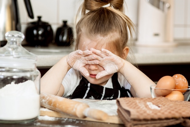 Маленькая девочка с подготовкой испечь домашний праздник пирог в кухне.