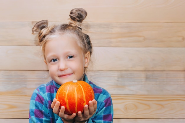 Little girl with a pumpkin in her hands on a background of wooden boards.